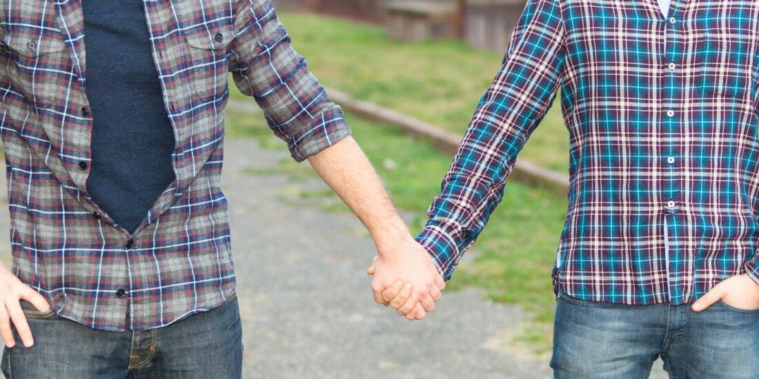 Body shot of two men in shirts and jeans holding hands