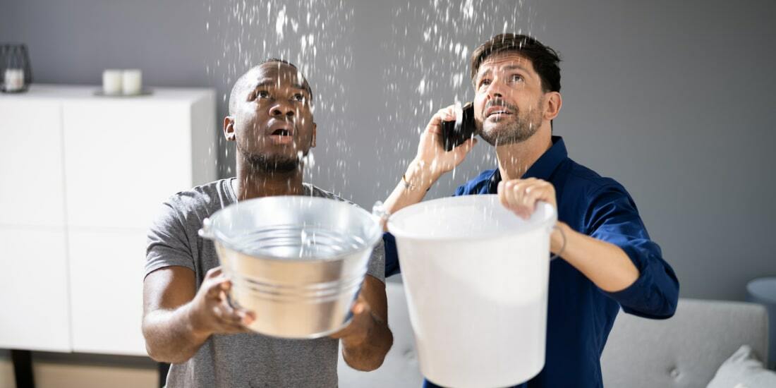 Two men with buckets catching water as it falls from the ceiling. One of them is also on the phone
