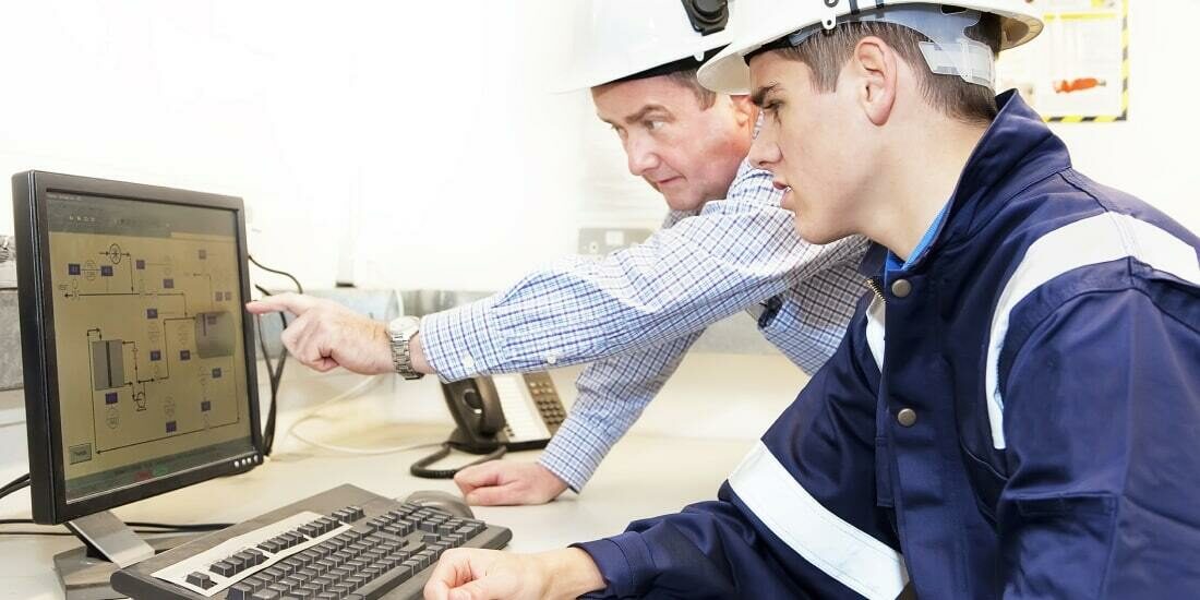 Two construction workers looking at floor plans on a computer screen