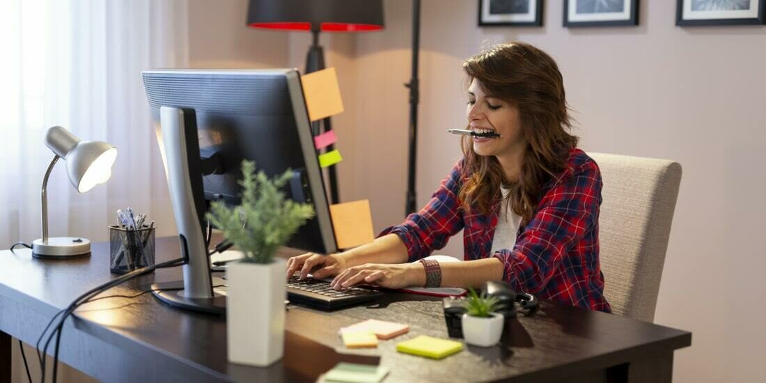 A female designer working at her desk with a pen in her mouth and post-it notes on the monitor
