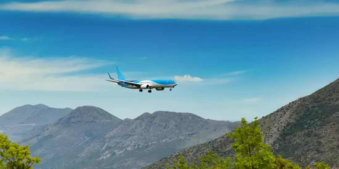 A blue and white plane beginning the landing procedure through a valley