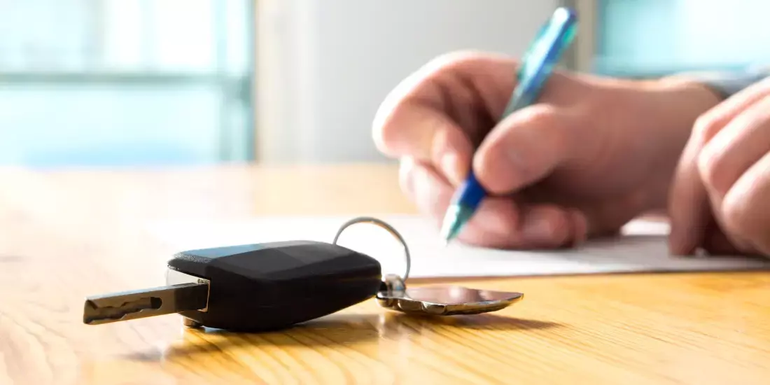 A man signing a contract with a set of car keys in the foreground