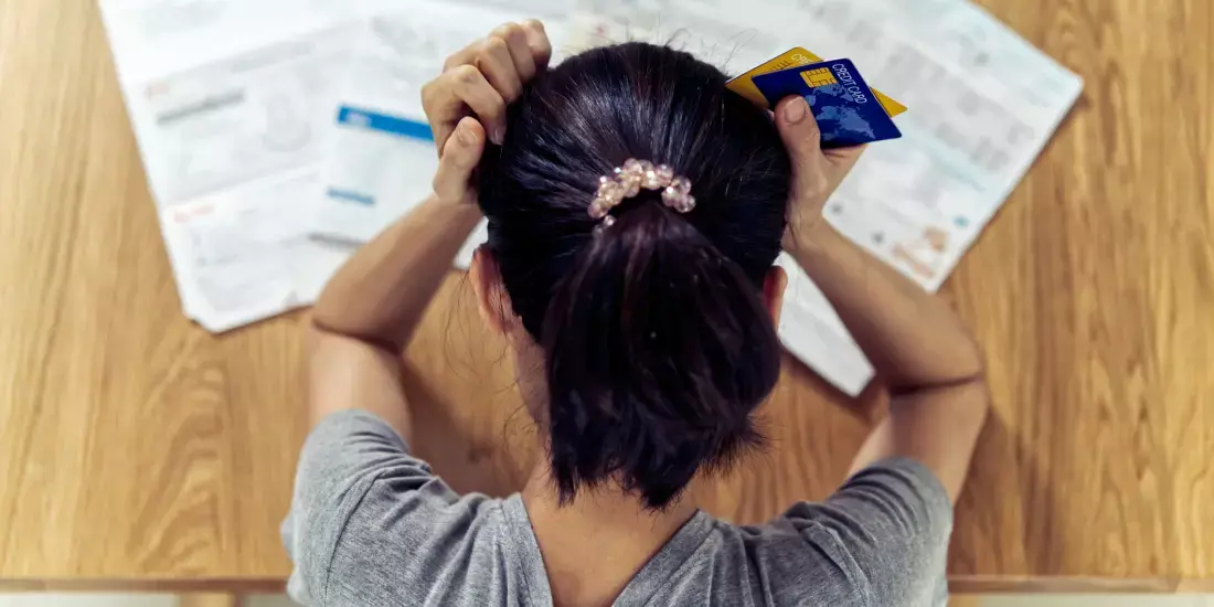 A stressed woman looking at documents with her hands on her head and a credit card in one hand