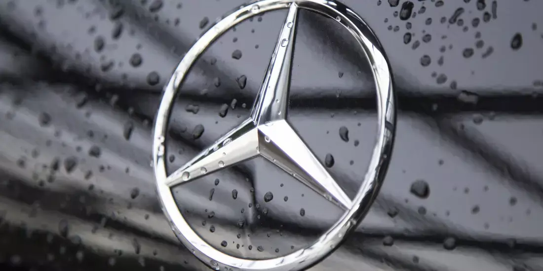 Close up of the Mercedes logo on a black vehicle with dew drops
