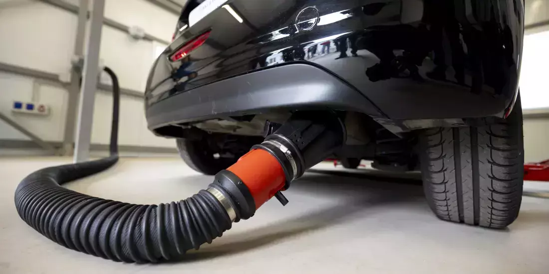 A black car has a pipe connected to its exhaust to test emissions