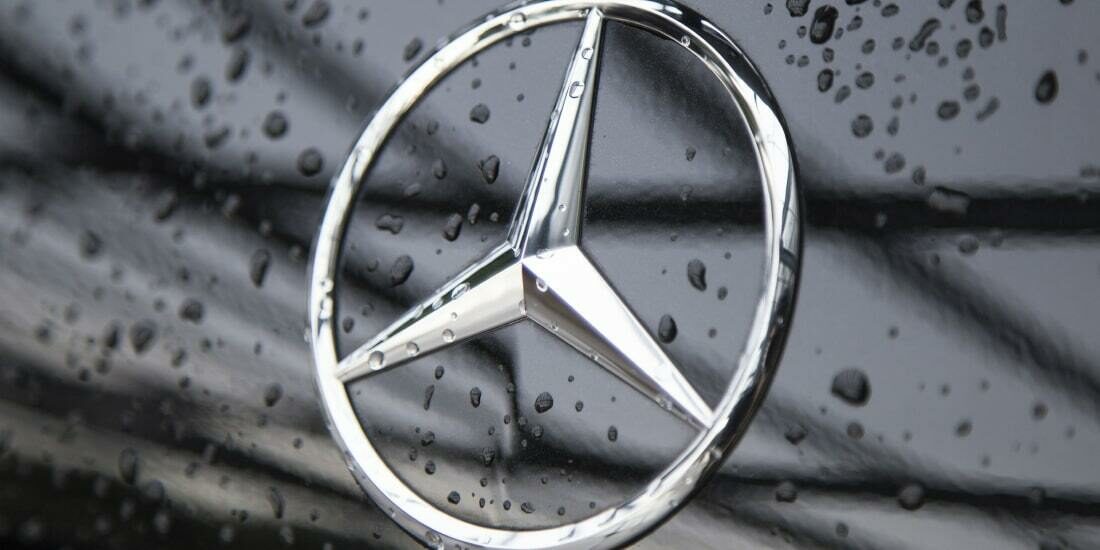 Close up of the Mercedes logo on a black car with some moisture on it