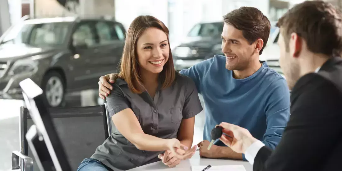 A young couple receiving the keys to their newly leased car by a sales person