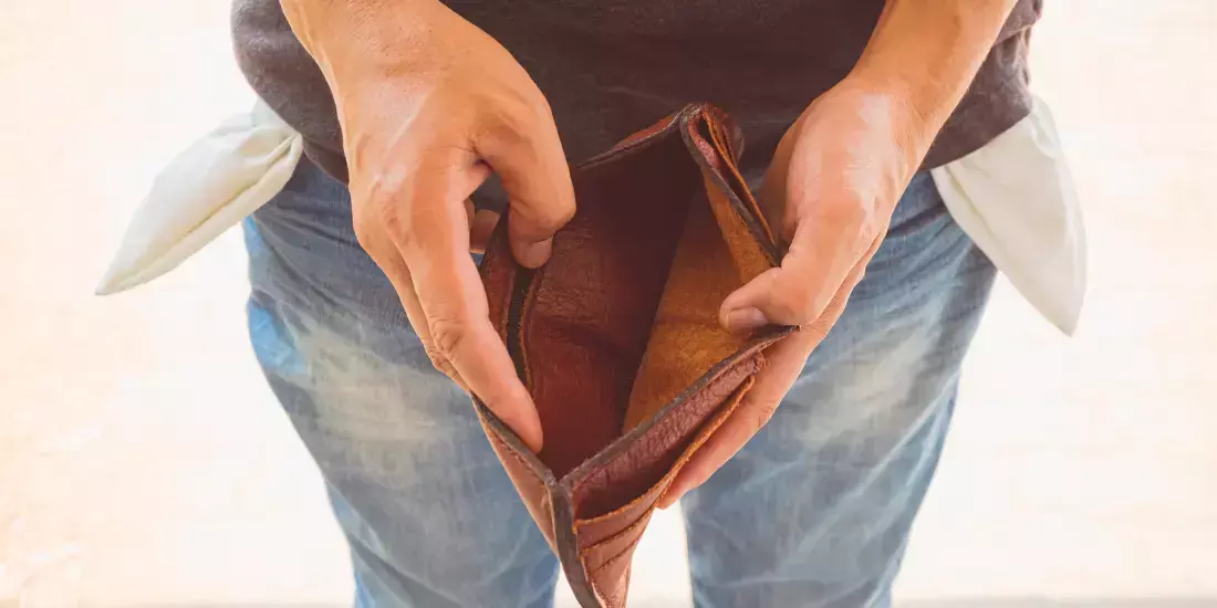 A man opens an empty wallet with outturned jeans pockets