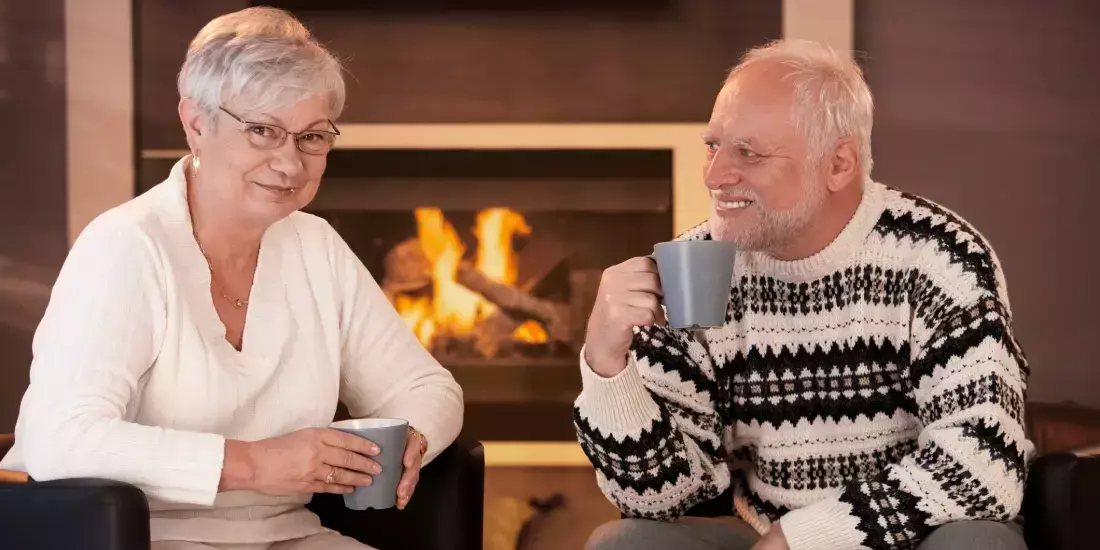 An old couple enjoying a drink together in front of a log fire
